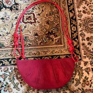 Red fabric half-moon crescent-shaped crossbody bag with a adjustable cord strap.